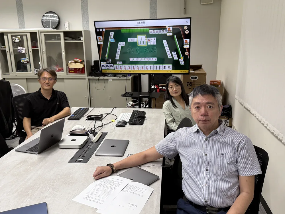 數位玩家團隊與高雄大學郭錦福老師進行麻將遊戲系統檢測，螢幕顯示極客麻將實機畫面